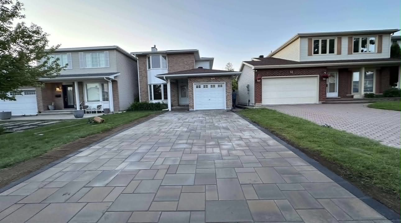 A finished multi-tone paver driveway running from the street to a two-car garage at dusk