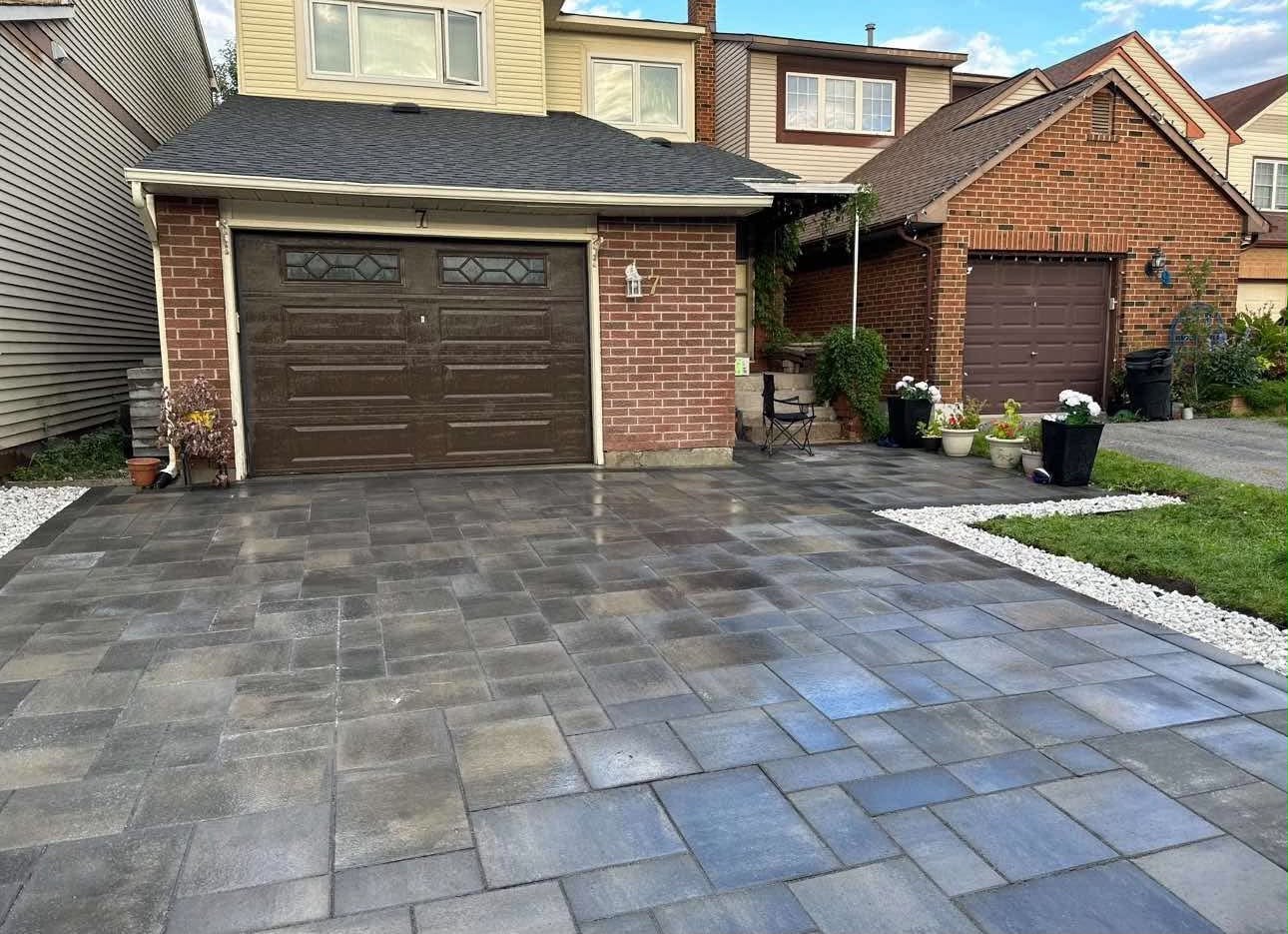 Dark charcoal and brown paver driveway leading to a garage, edged with white river rock