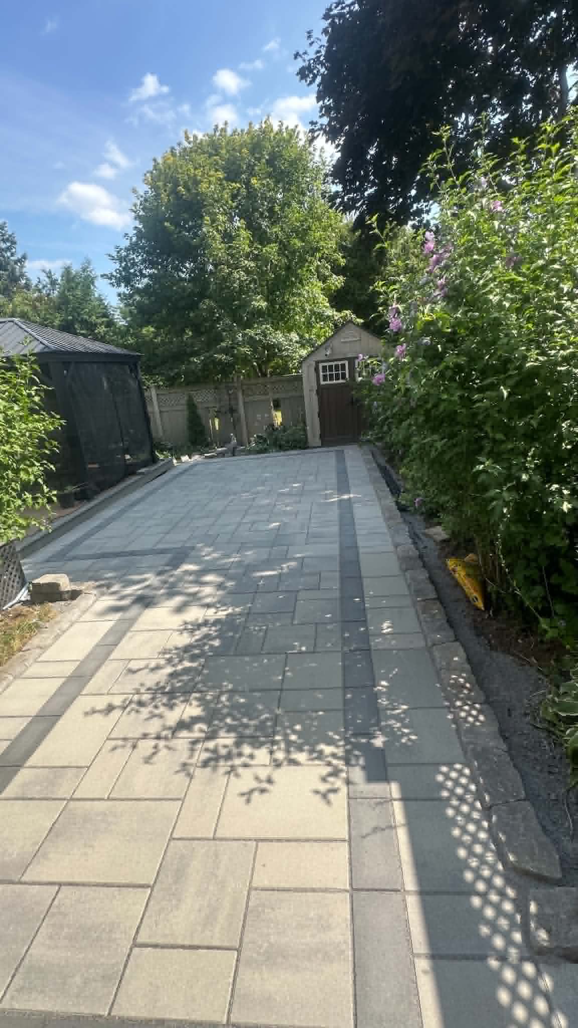Shaded paver laneway with a charcoal ribbon running between garden beds to a detached garage