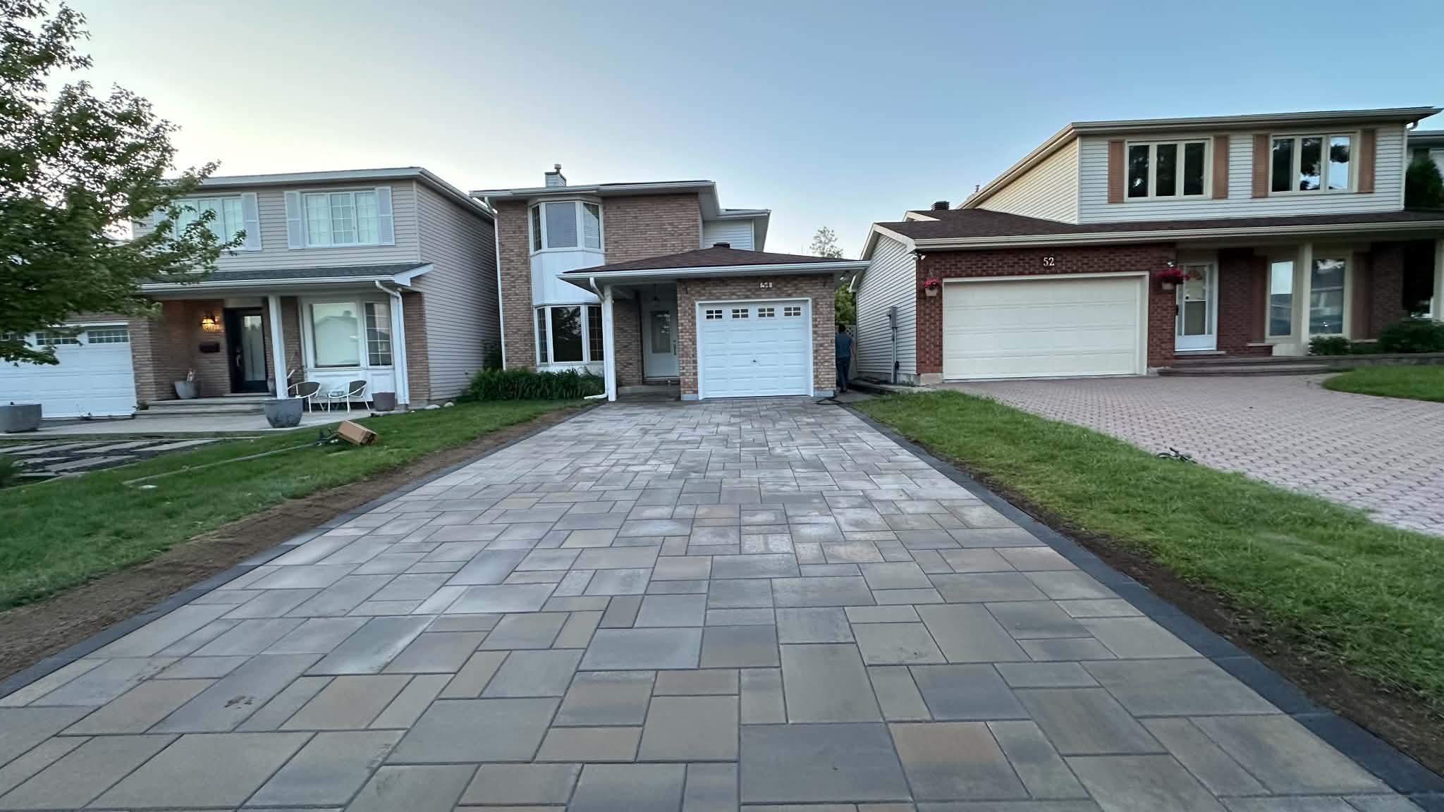 Freshly laid tan and grey paver driveway with a charcoal border running between two lawns