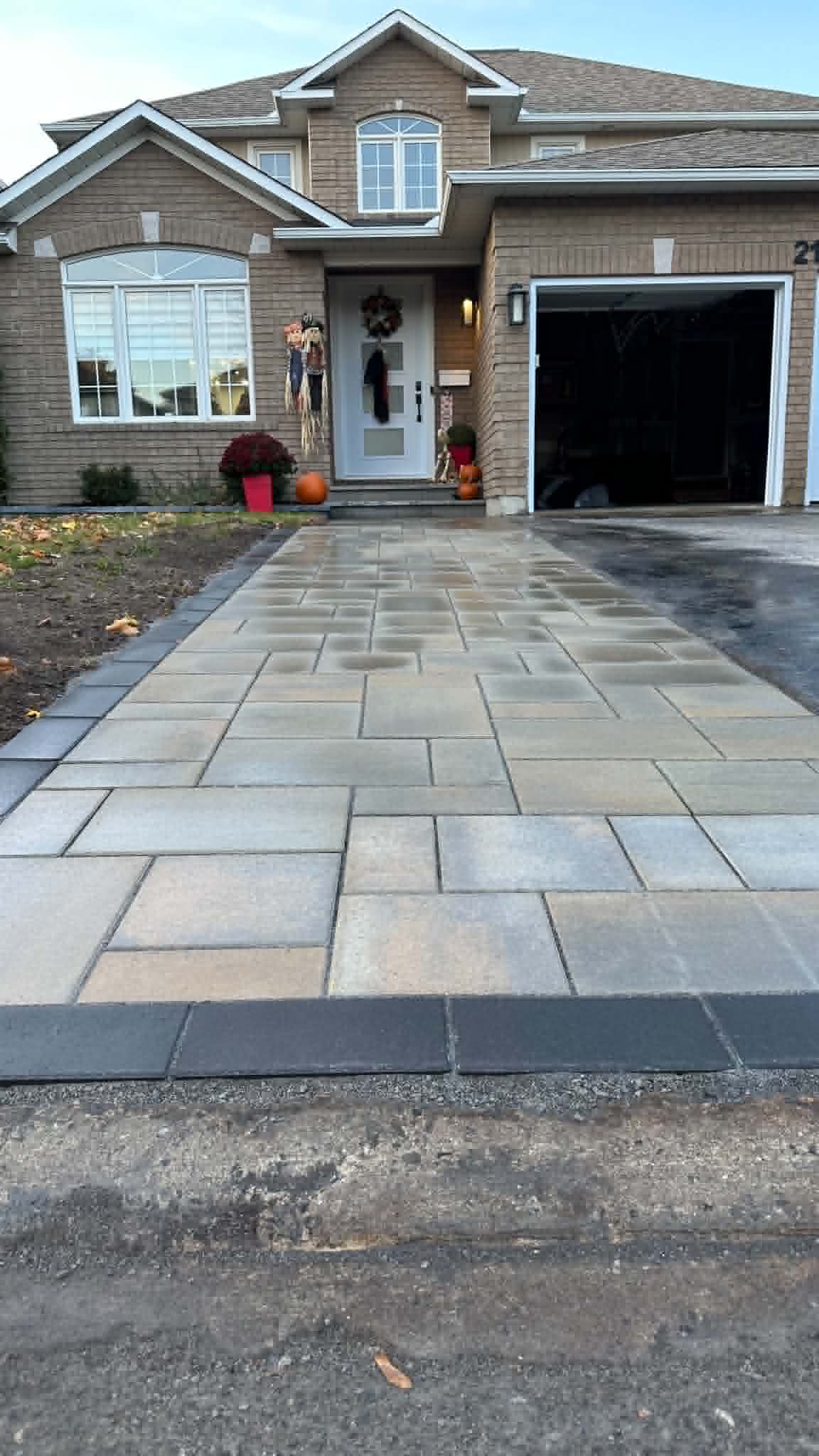 Wide tan-blend paver drive with a charcoal edge meeting the asphalt half of a shared driveway