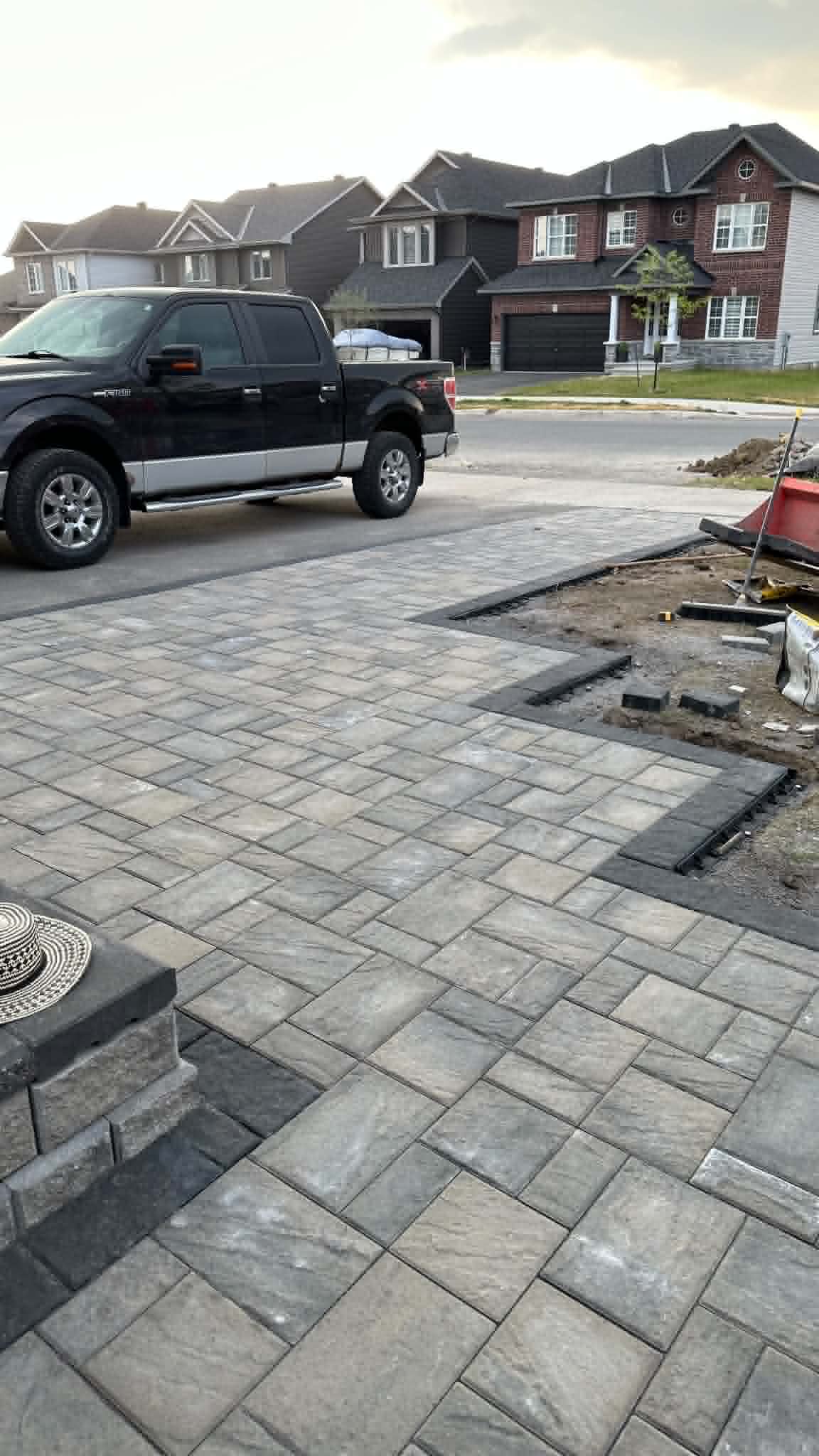 Slate-textured paver parking court wrapping around a stone pillar, mid-install