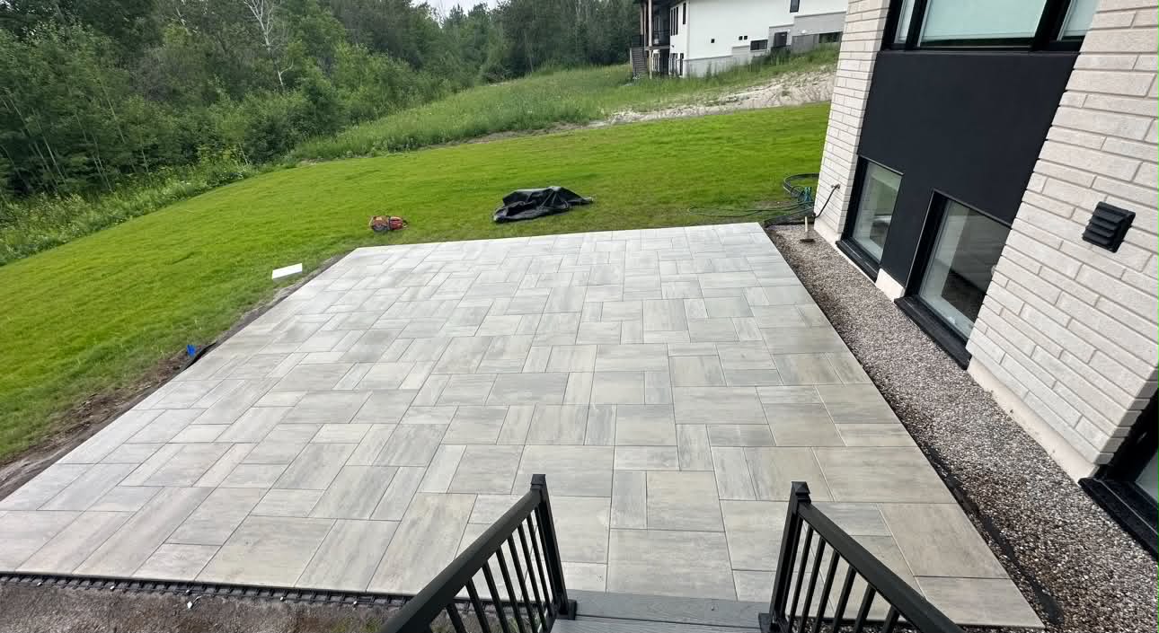 Large-format grey slab patio cut into a sloped lawn beside a modern brick house