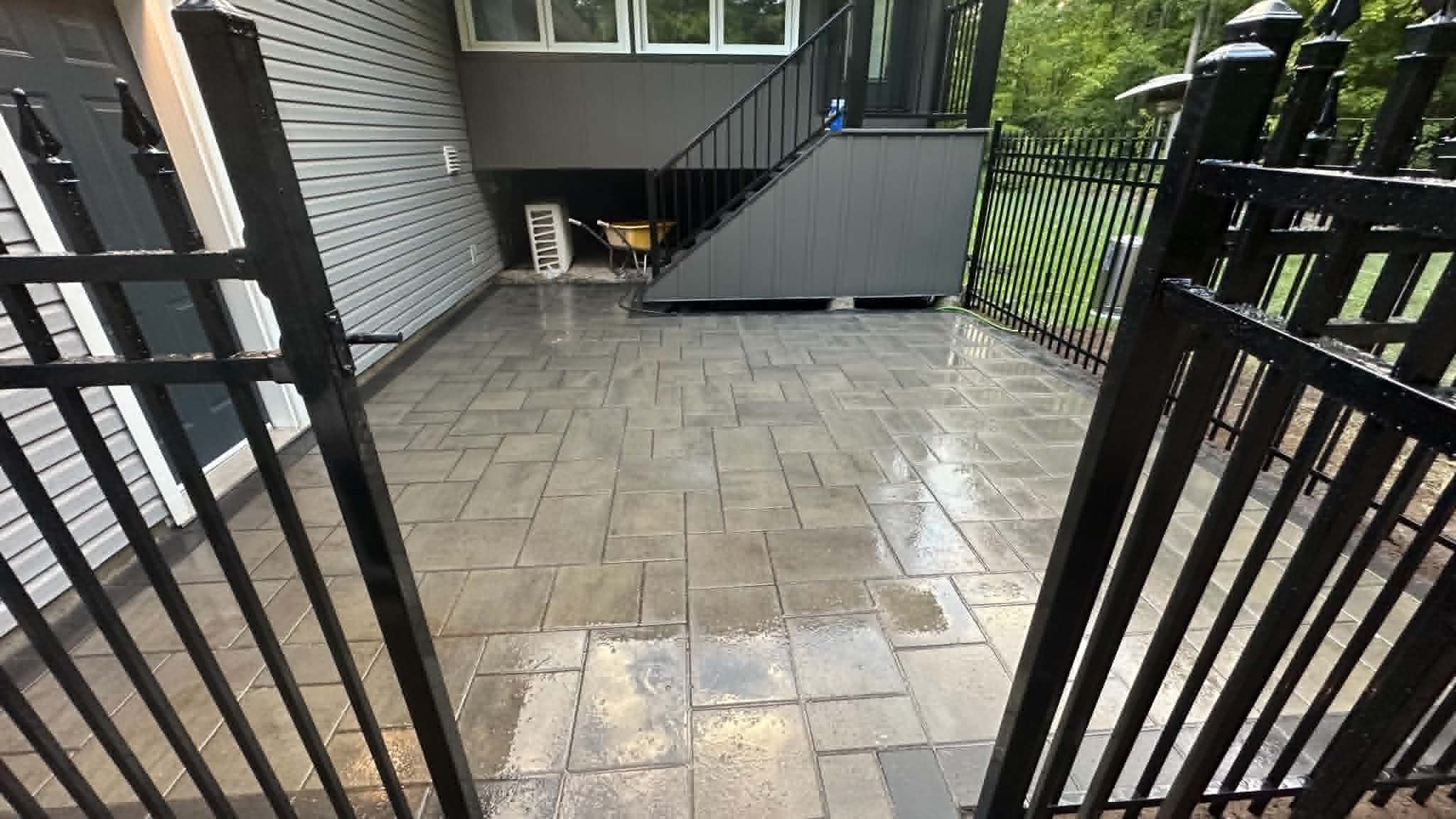 Herringbone-laid grey patio behind a black iron gate at the side of a house