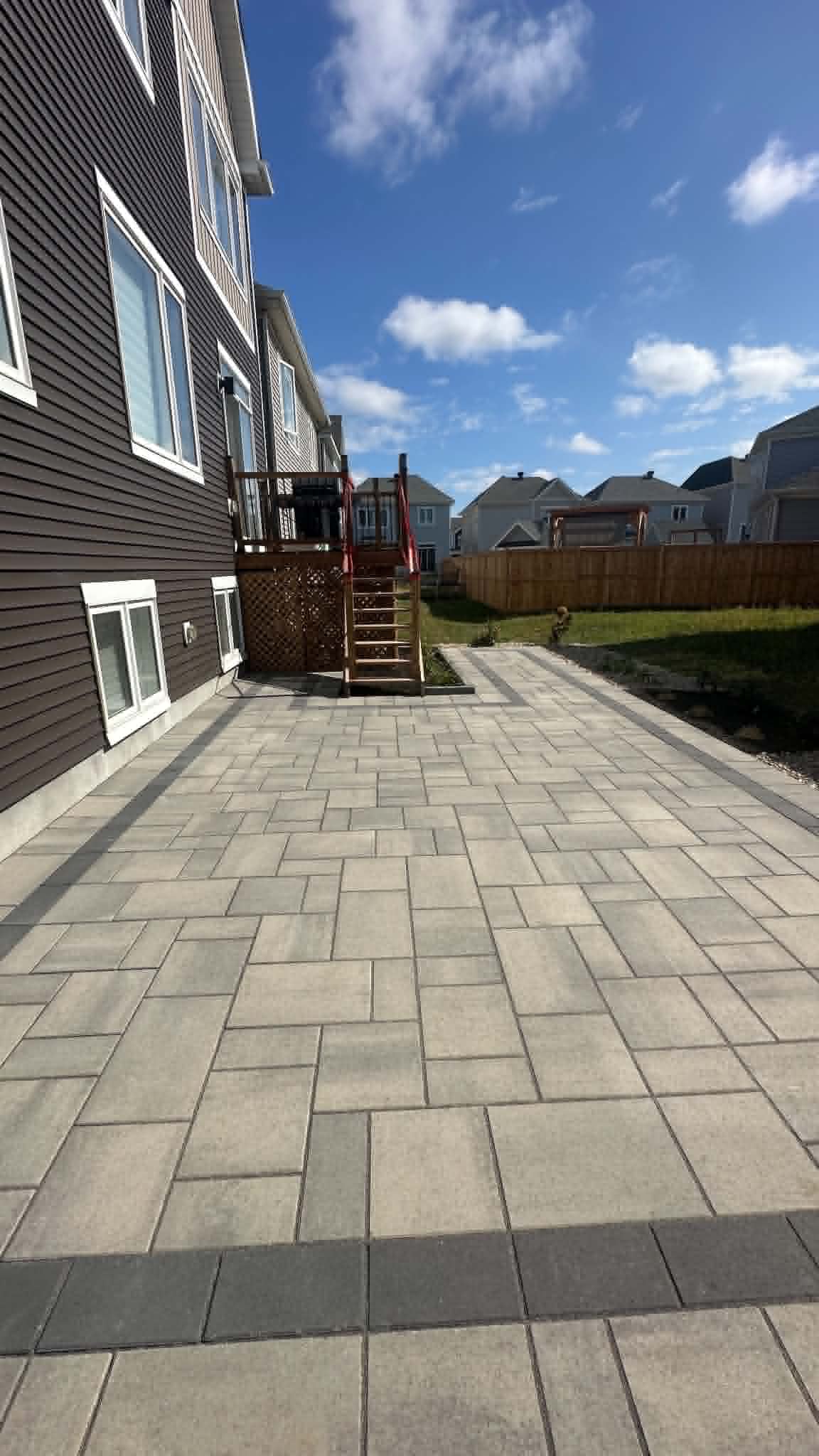 Wide side-yard paver patio with a charcoal band running back to a cedar deck stair