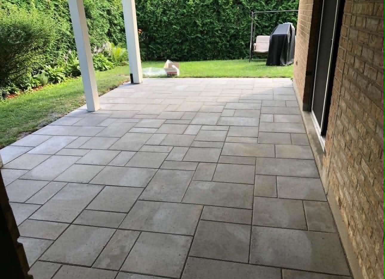 Beige large-format slabs laid under a covered rear porch next to a cedar hedge
