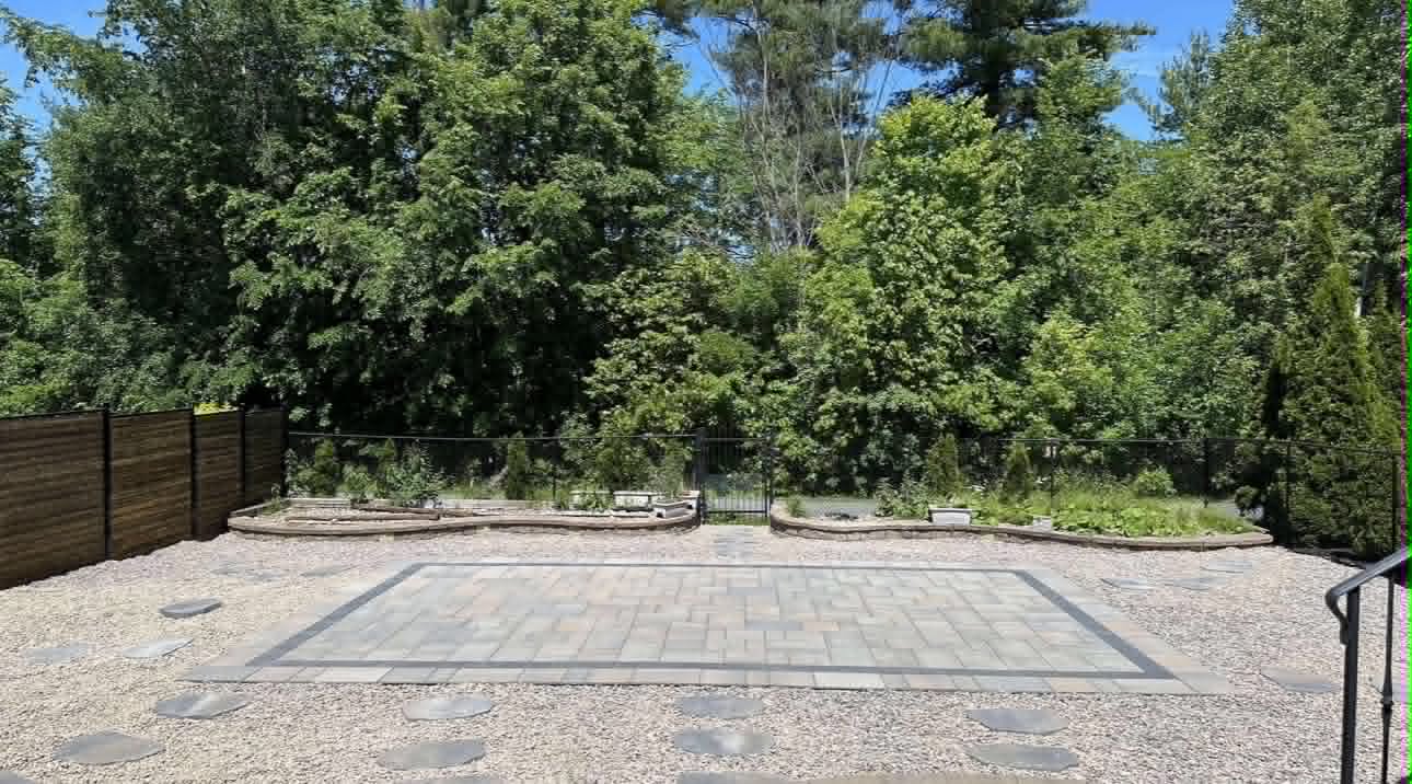 Bordered paver pad set in pea gravel with flagstone stepping stones, backed by trees
