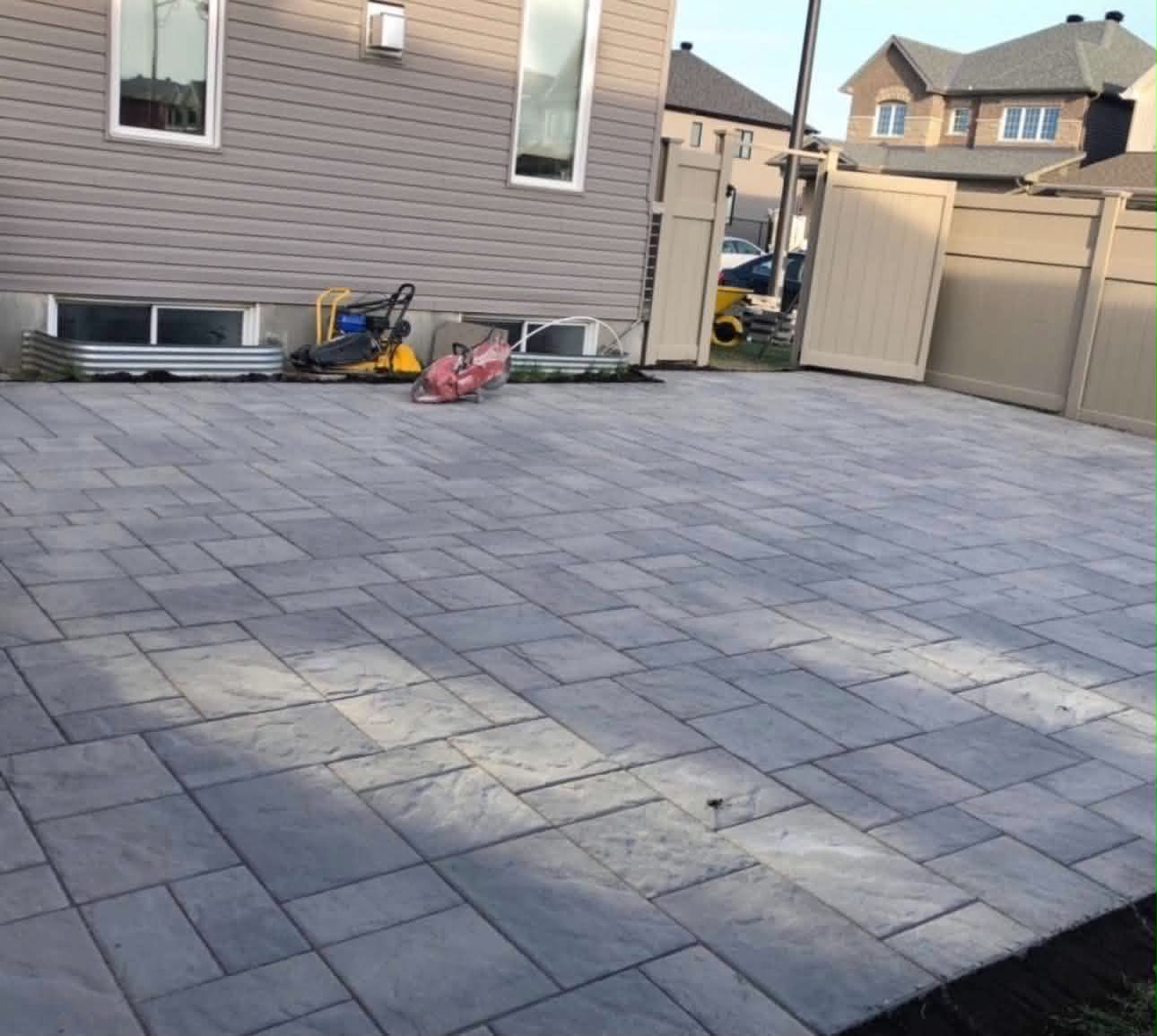 A freshly laid grey paver patio with a plate compactor and wet saw still on the surface