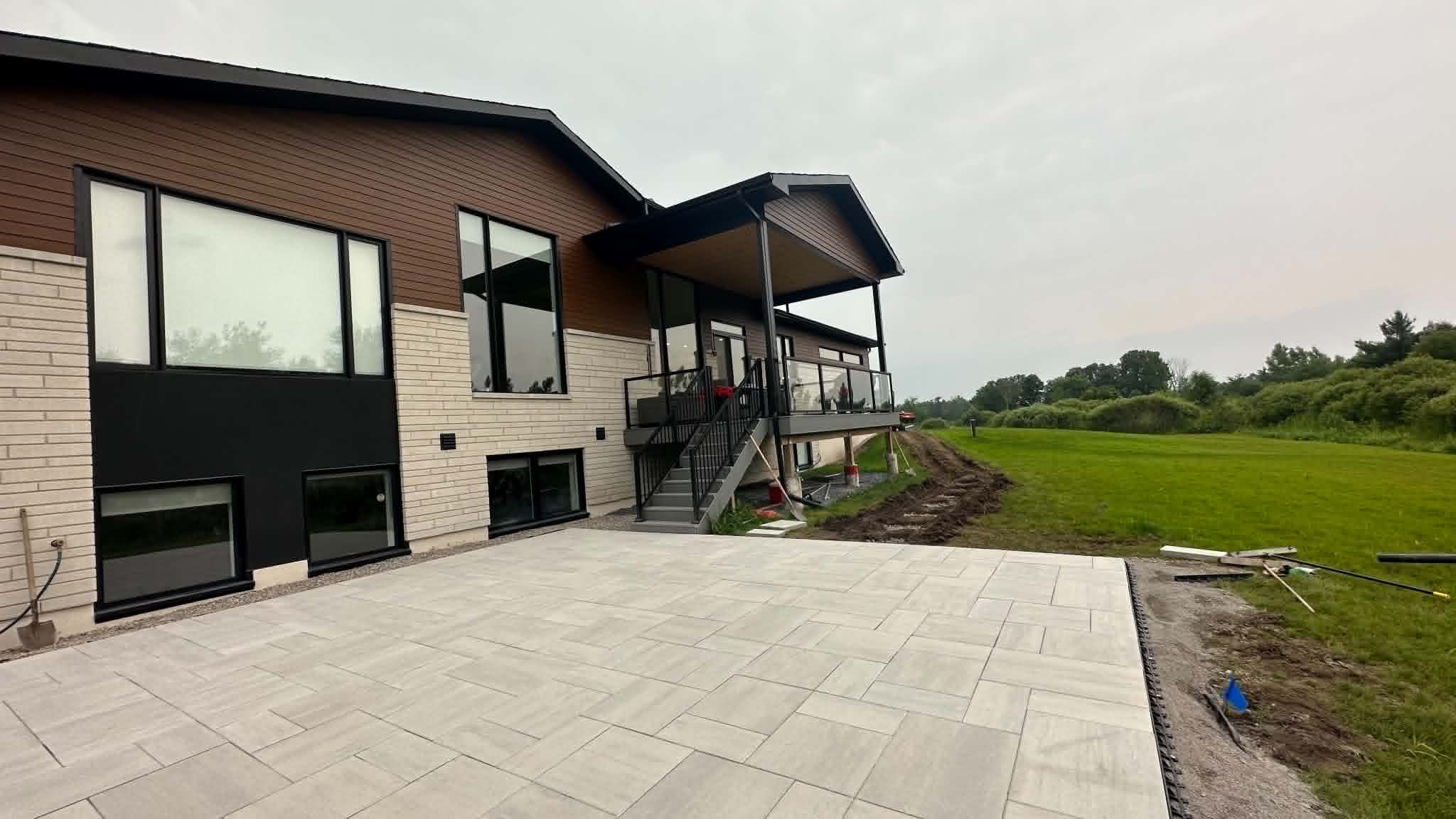 Large light slab patio being laid behind a modern new build with a raised deck and stairs