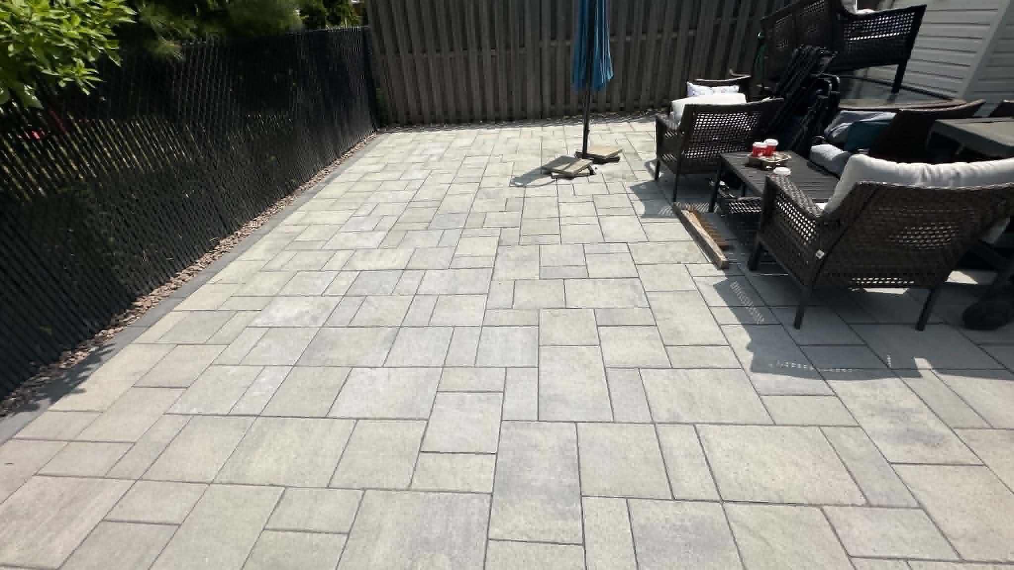 Grey slab patio with a charcoal border along a privacy-slat fence, furnished with a patio set and umbrella