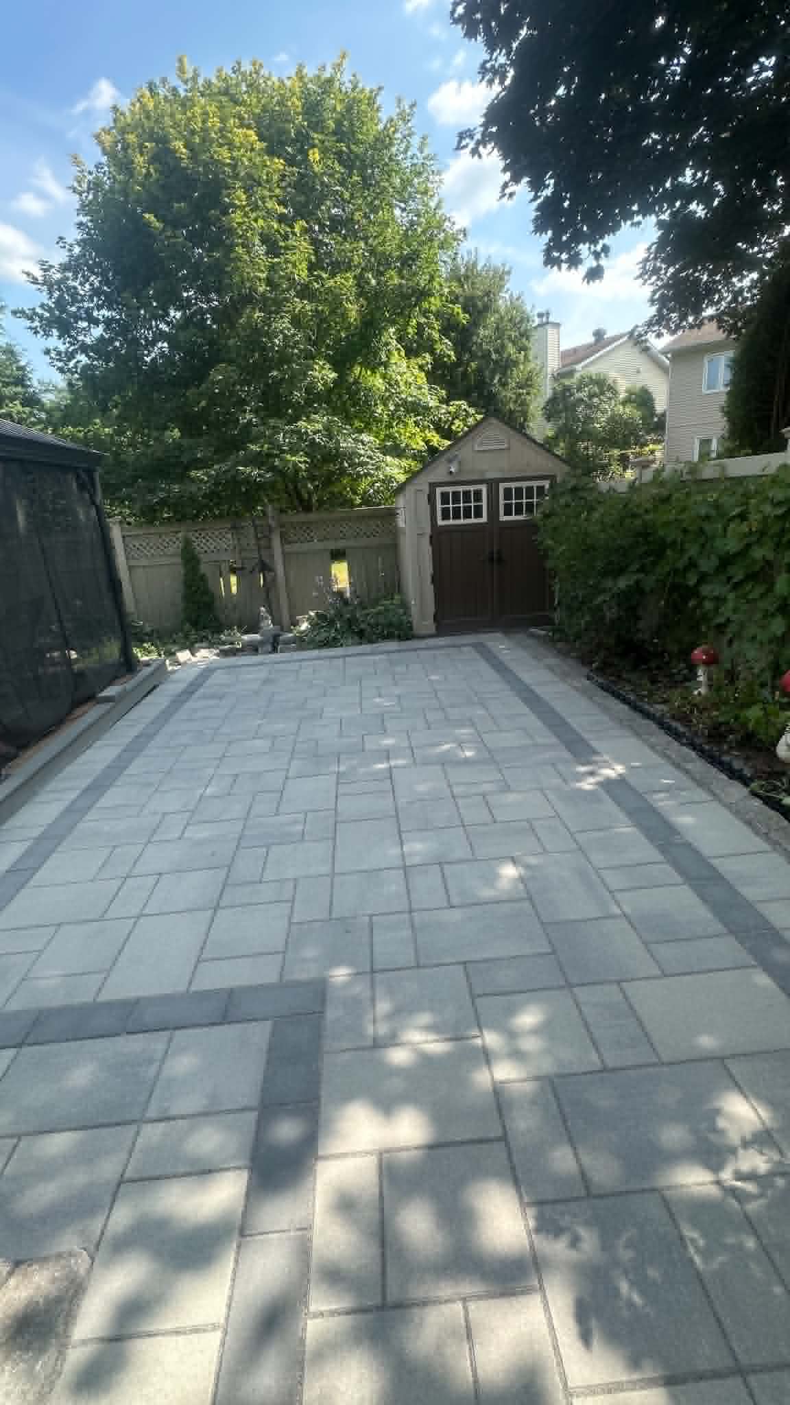 Light grey paver patio with double charcoal bands leading back to a garden shed