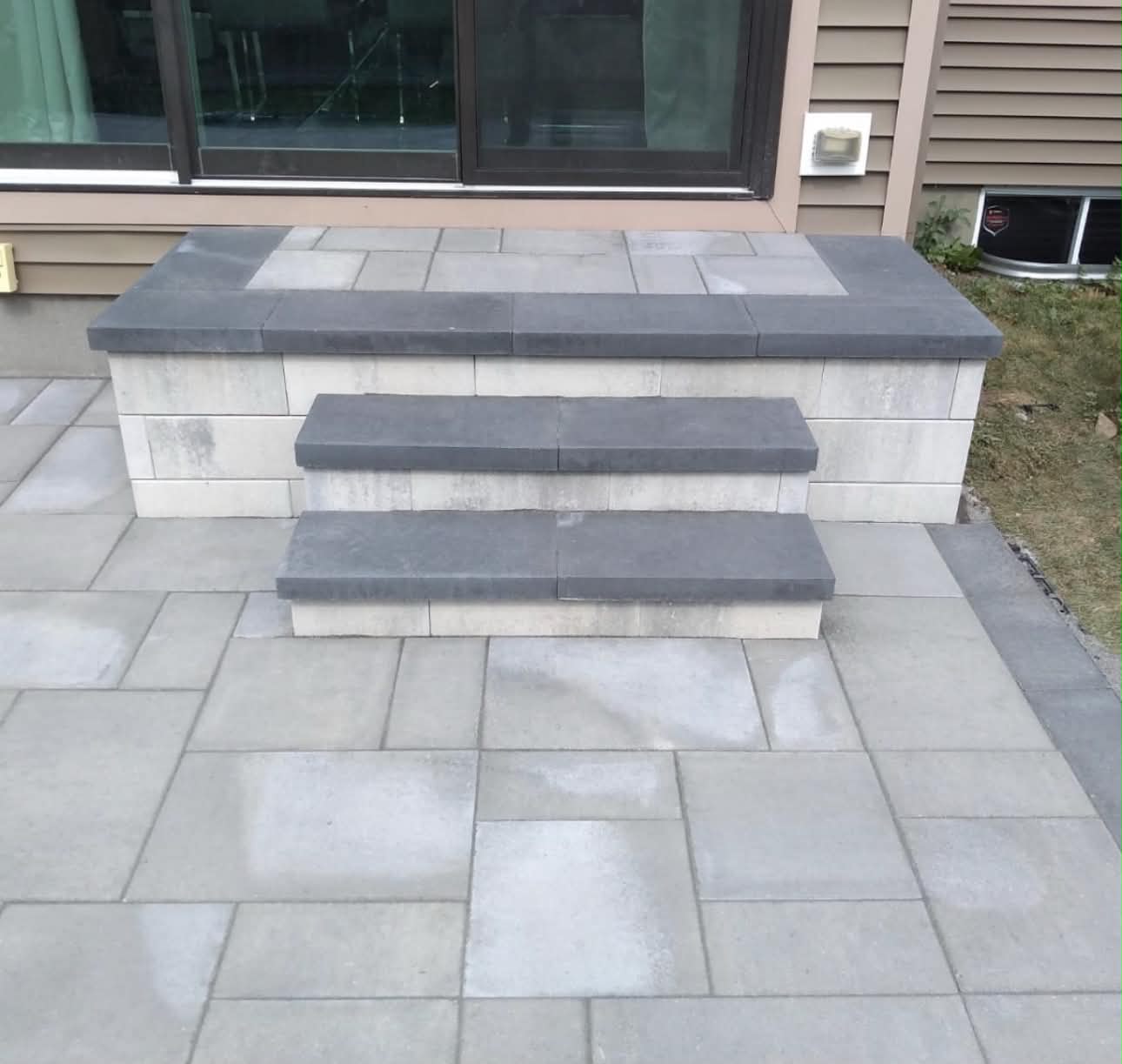Charcoal-capped seat wall and two paver steps at a patio door, built from light block