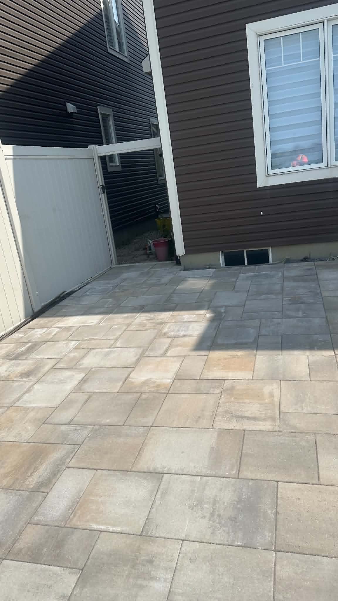 Beige slab patio running to a white privacy gate at the side of the house