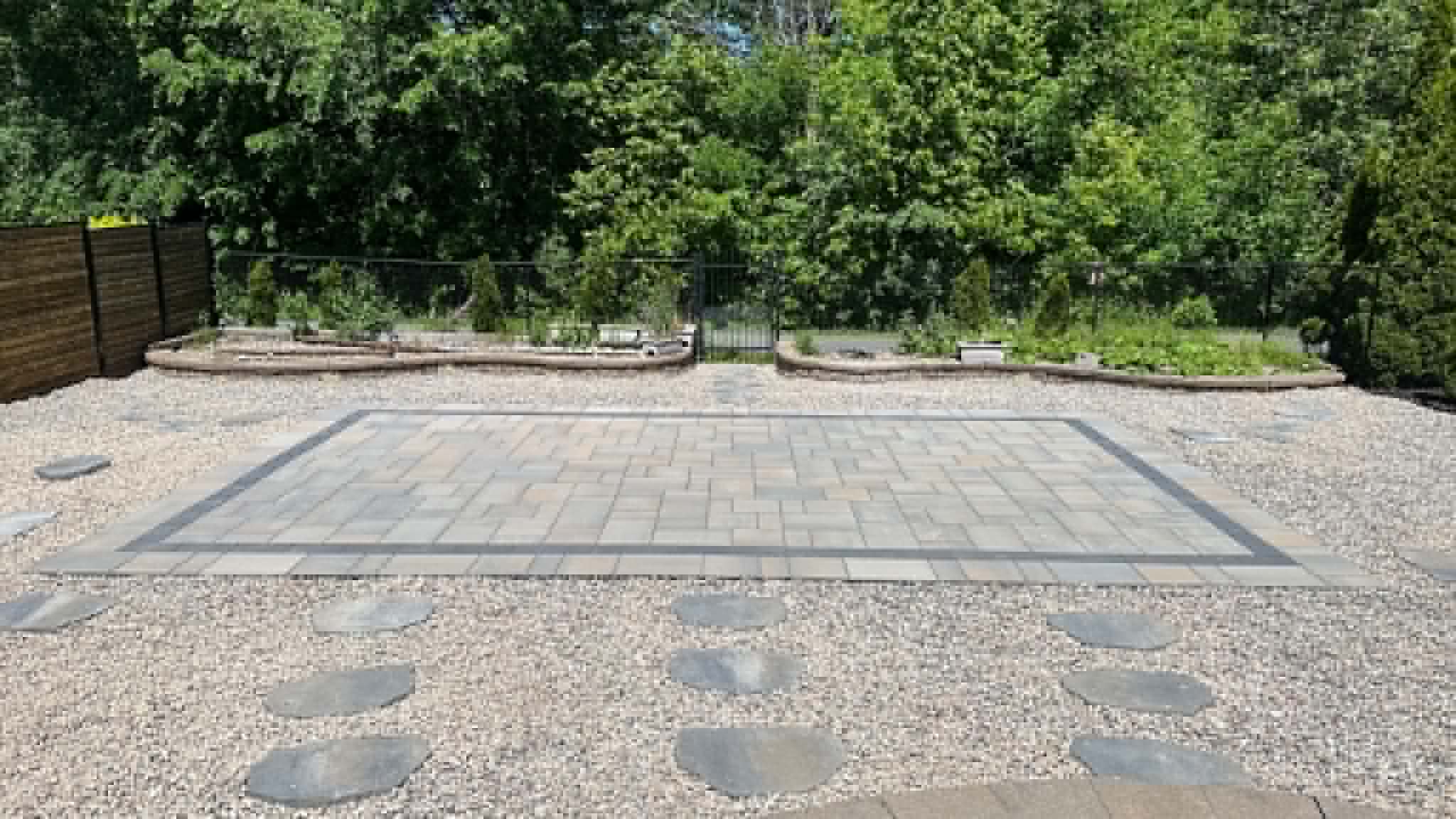 Bordered paver pad set in pea gravel with flagstone stepping stones and low garden walls behind