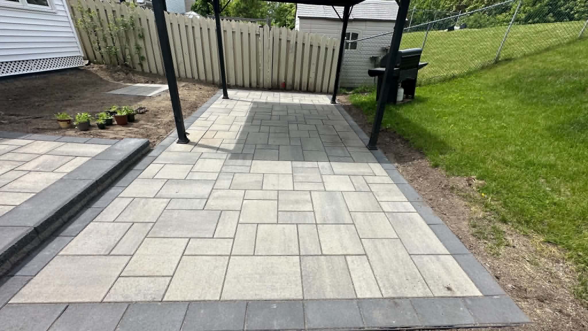 Light slab pad with a charcoal border under a gazebo, stepping down from the main patio
