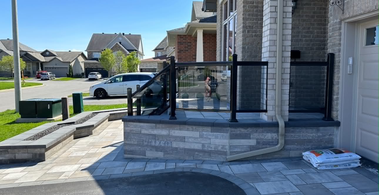 Raised front entrance faced in stacked stone with a glass railing and paver steps