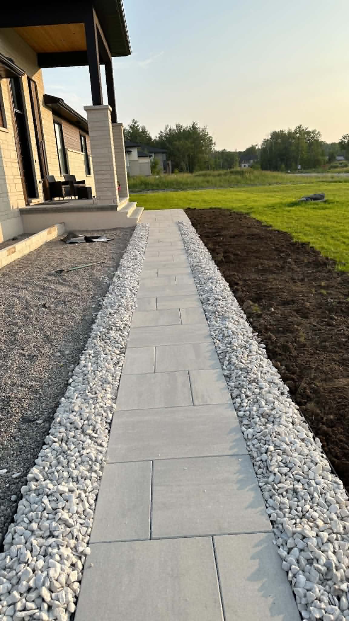 Straight grey slab walk flanked by white decorative stone along the front of a modern home