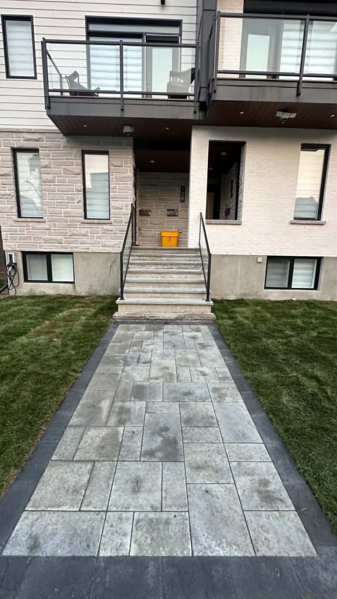 Grey slab walk with a charcoal border crossing new sod to townhouse entrance steps