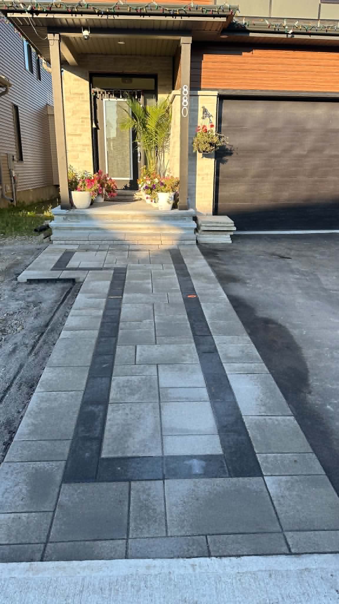 Grey front walk with dark banding running along the asphalt driveway to porch steps
