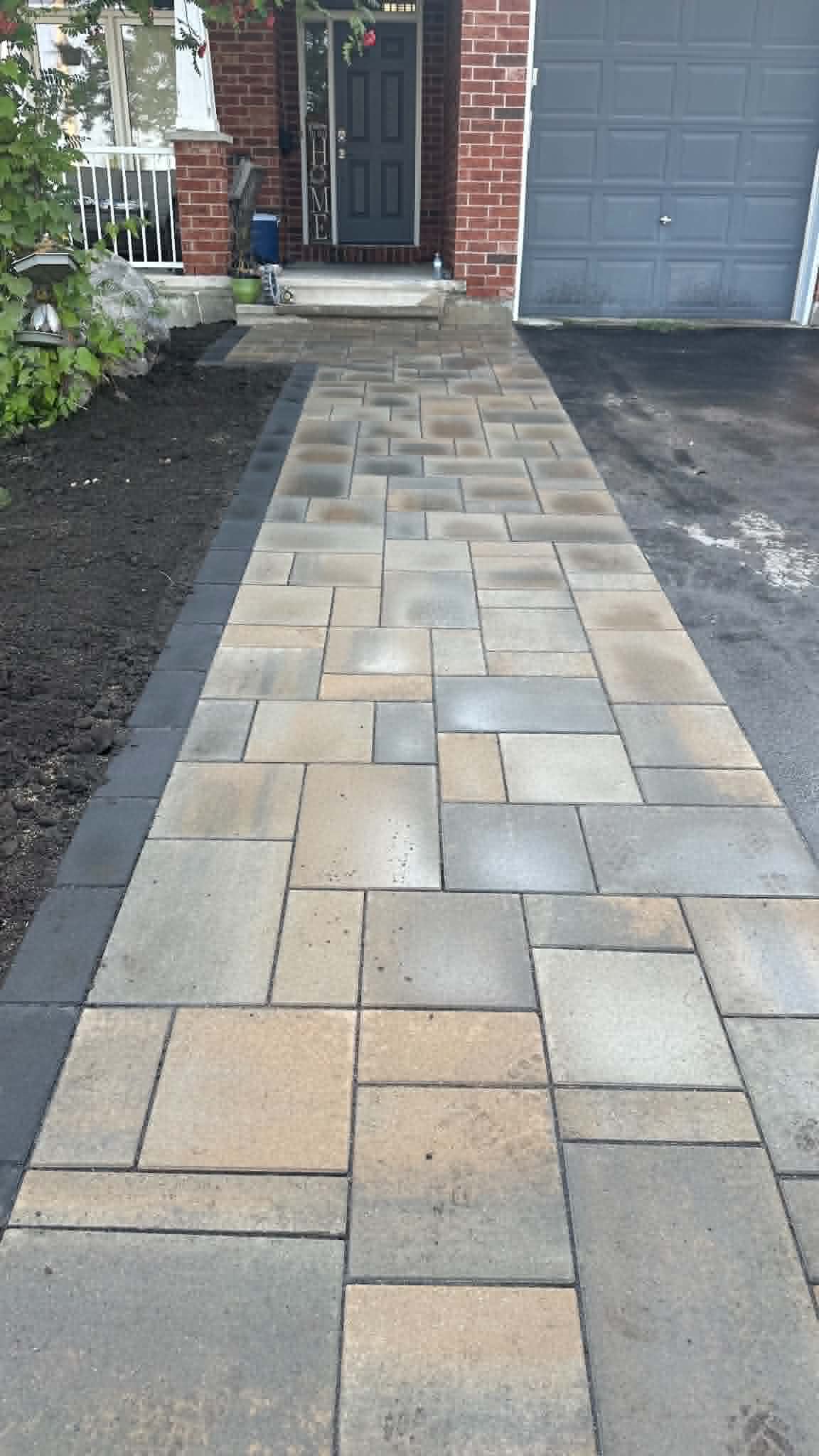 Tan and grey blend walkway with a charcoal border between the garden bed and asphalt driveway