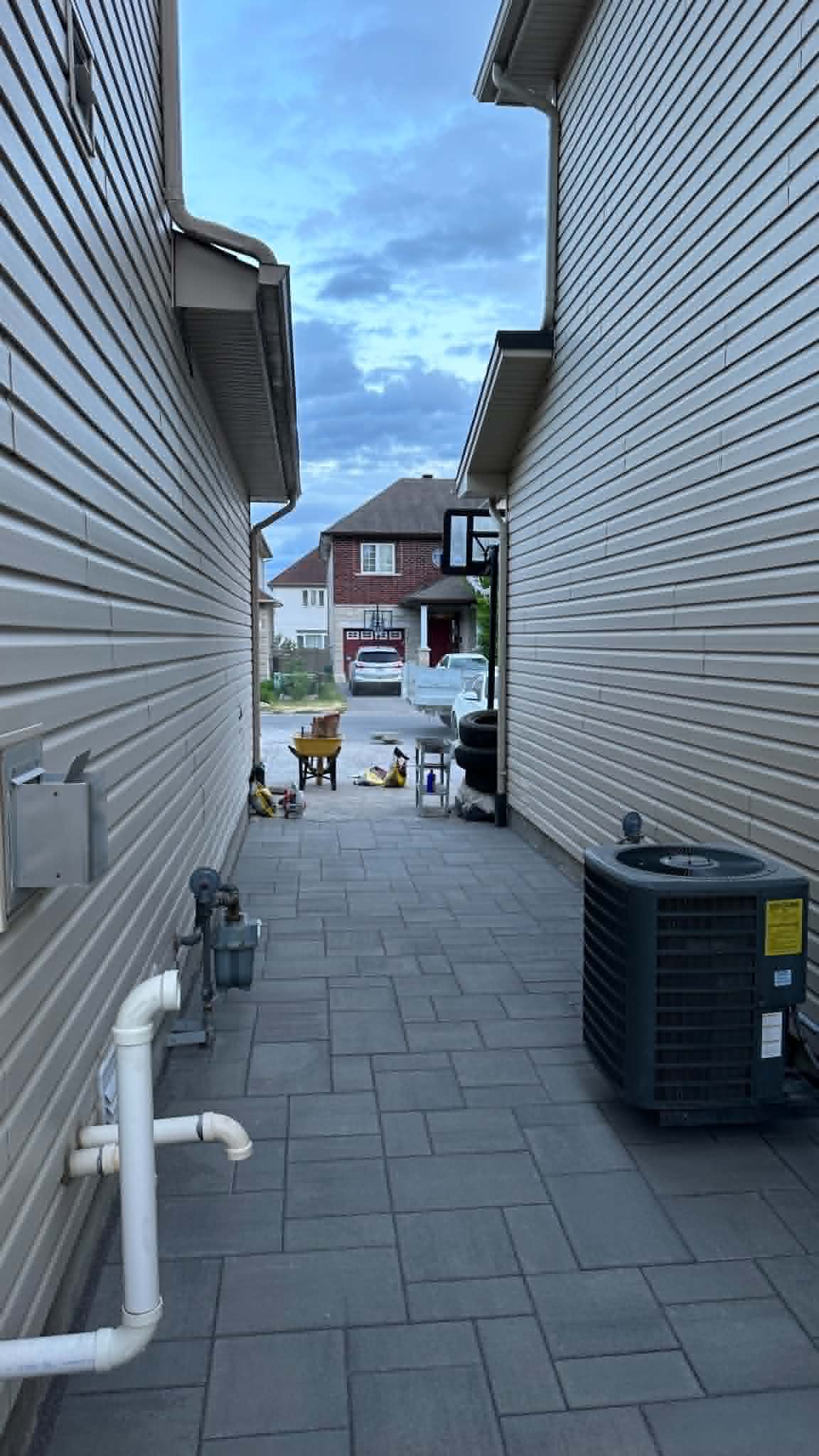 Narrow grey paver walkway running between two houses toward the street