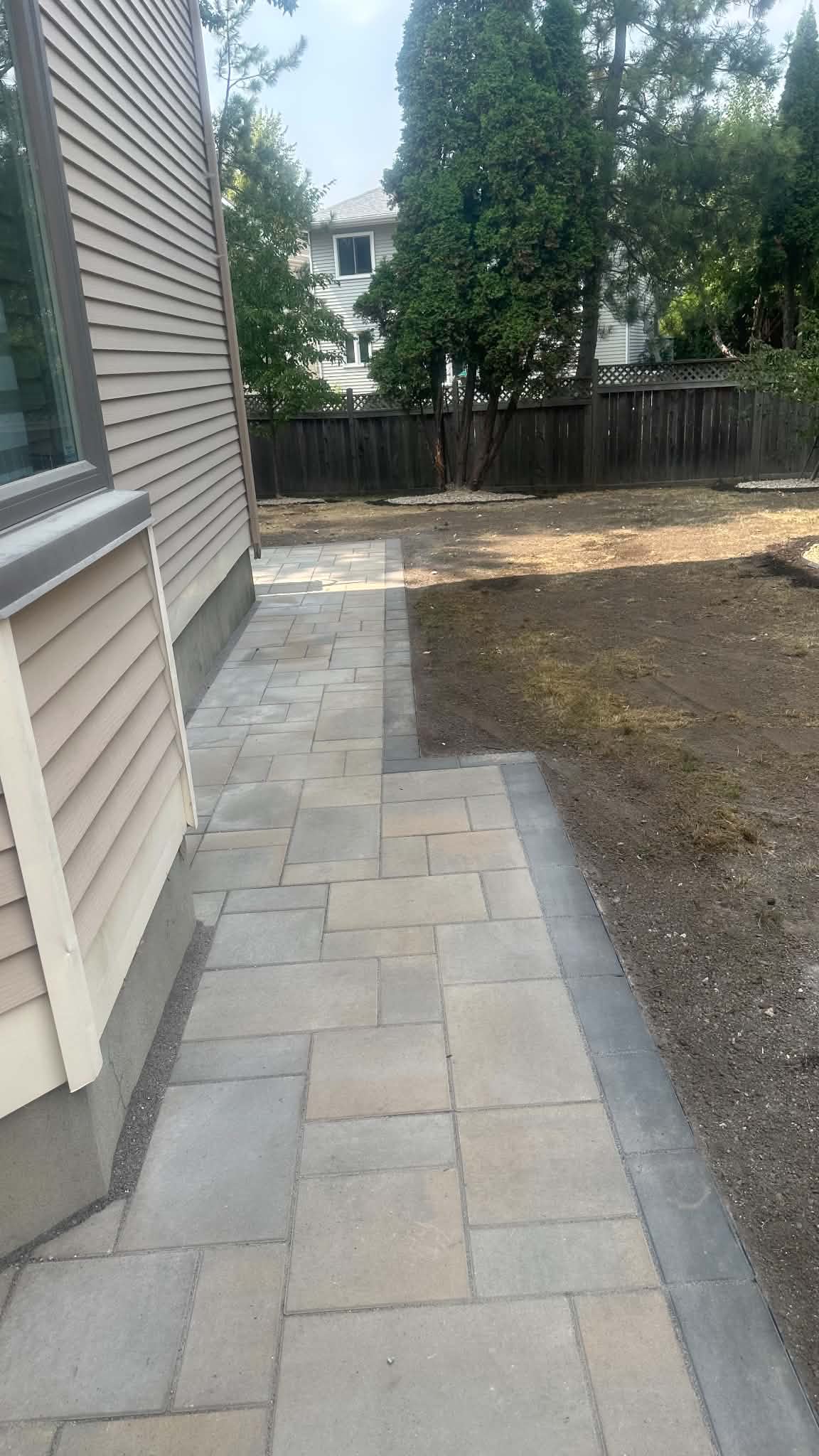 Beige and grey slab walkway with a charcoal border wrapping the back corner of the house