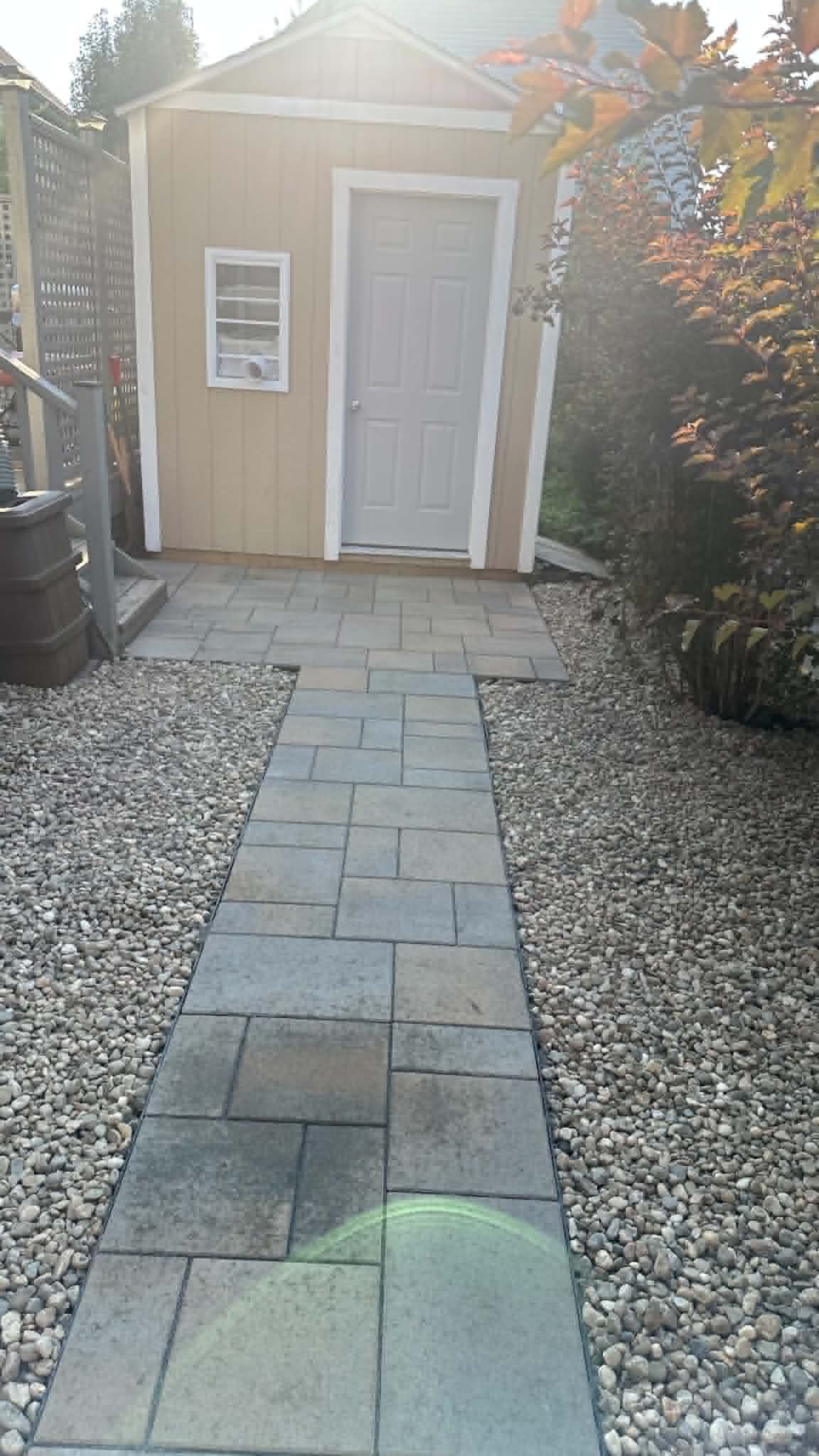 Slab walkway through river rock leading from deck steps to a garden shed door