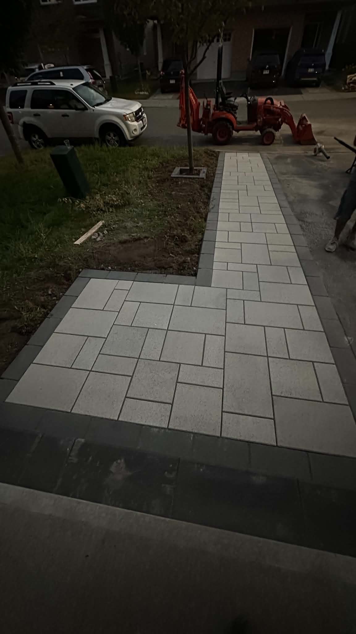 L-shaped white slab walk and pad with a charcoal border at the front of the house at dusk